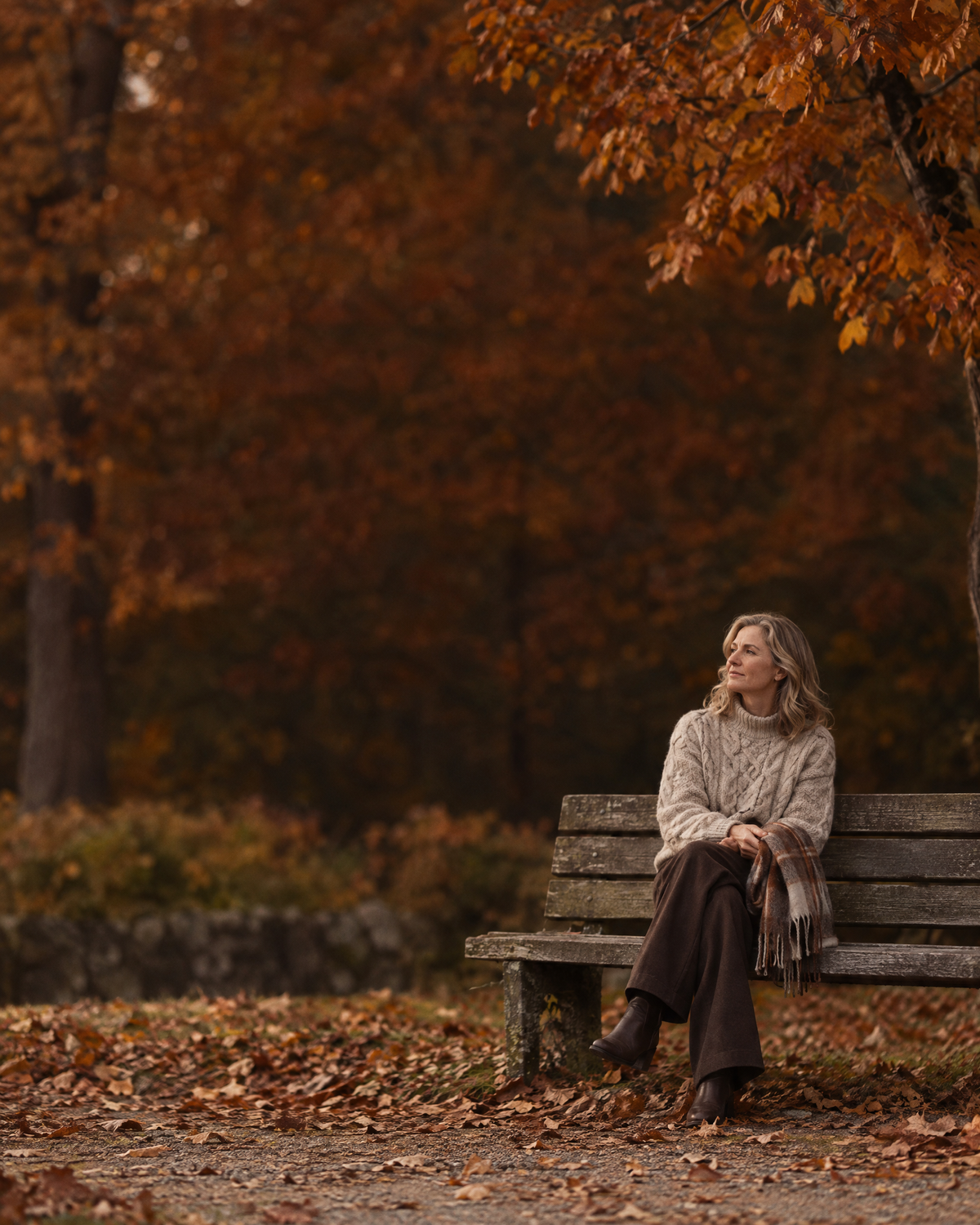 Frau im Zopfstrick-Pullover auf einer Parkbank im Herbstlaub